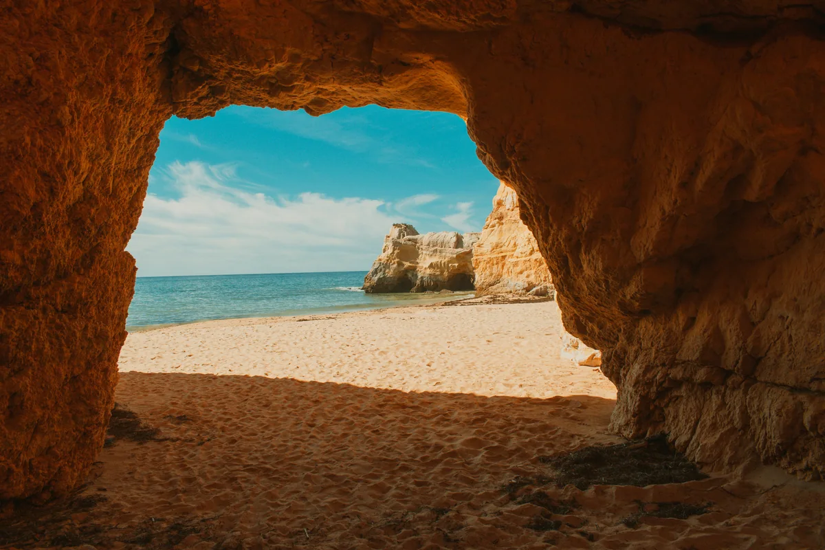 A sea cave opening onto a quiet beach and blue water