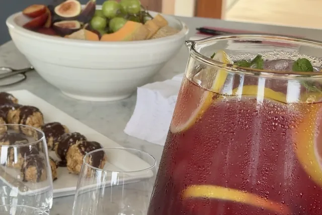 A pitcher of sangria, fresh fruit and cookies on a marble counter
