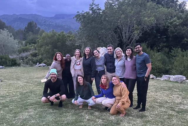 Twelve retreat participants together on the grass at dusk, mountains behind them
