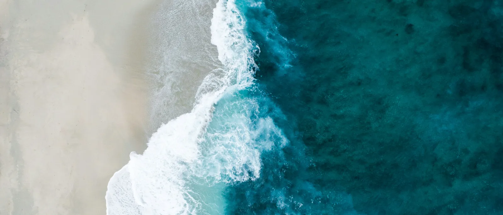 Surf meeting a pale shoreline, seen from directly above